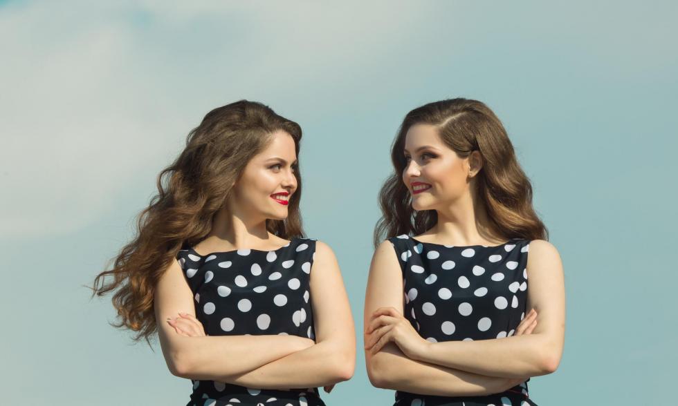 Zwei sich aehnelnde junge Frauen in schwarzen weiß gepunkteten Keidern schauen sich gegenseitig an