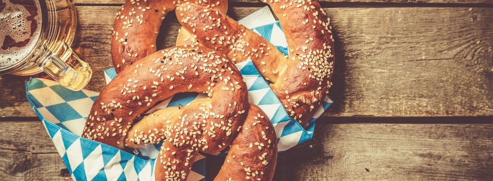 Brezeln auf blau-weißen Servietten und Bier auf einem Holztisch