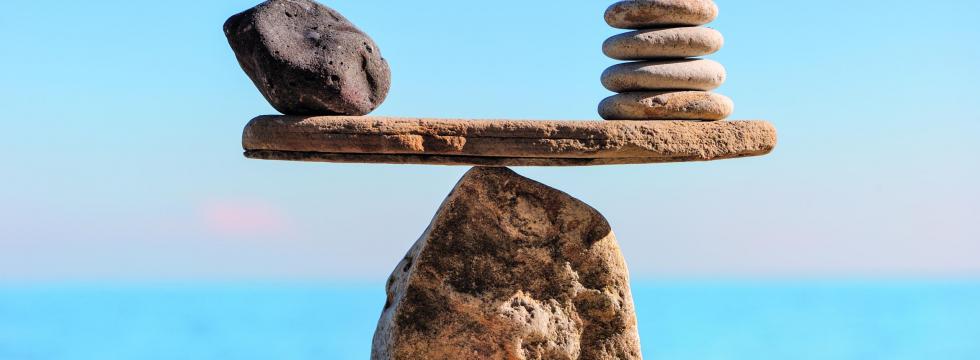 Ein Stein am Strand mit einer Spitze balanciert einen flachen Stein auf sich, der wiederum jeweils links und rechts weitere Steine auf sich balanciert.