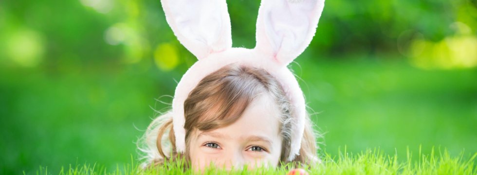 Mädchen mit Hasenohren auf einer Wiese mit Ostereiern