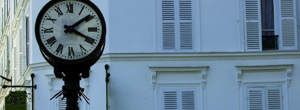 Antike Uhr vor einem Altbau und einem Café-Schild