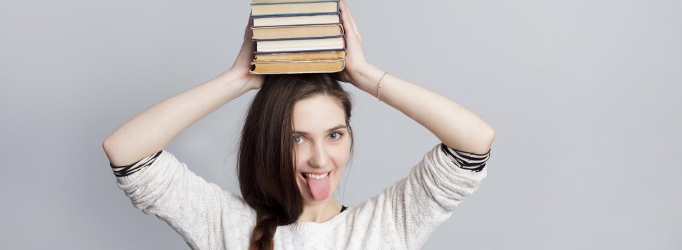 junge Frau mit Büchern auf dem Kopf und ausgestreckter Zunge