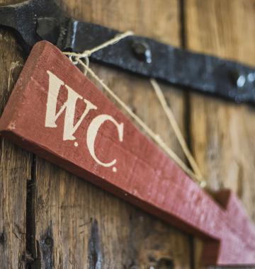 Pfeil aus Holze mit Aufrschrift "W.C." hängt auf einer Holzwand