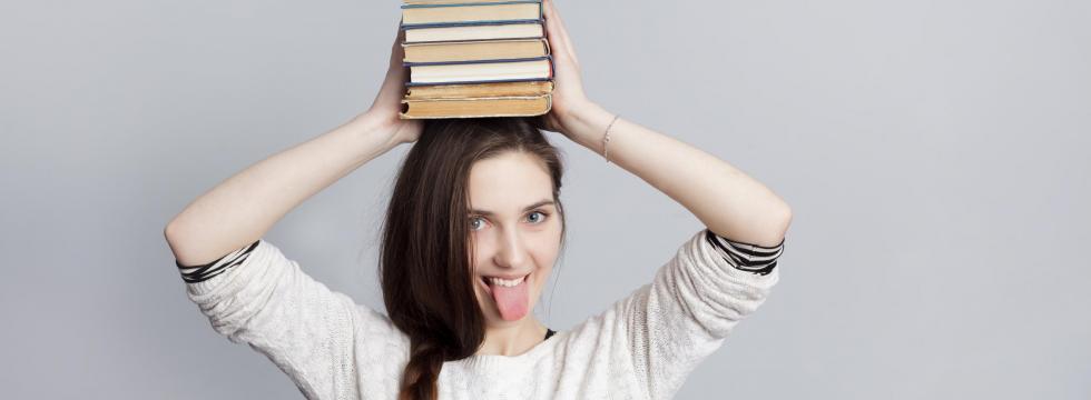 junge Frau mit Büchern auf dem Kopf und ausgestreckter Zunge