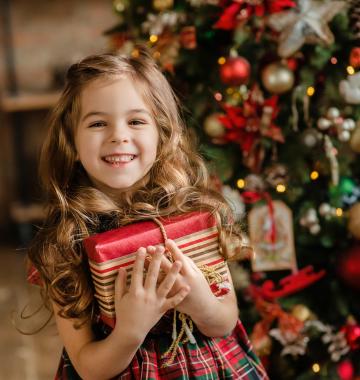 Mädchen mit einem Geschenk neben einem Weihnachtsbaum