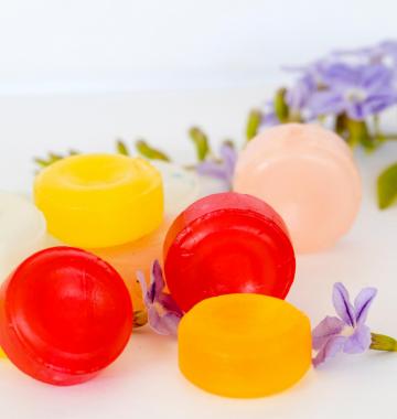 Hustenbonbons in rot, gelb, weiß und hellgrün liegen neben dekorativen Blüten.