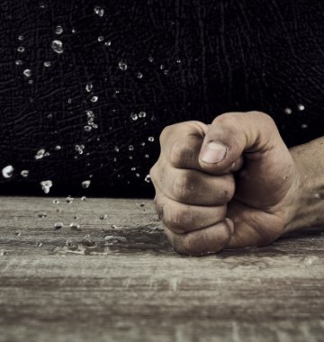 Eine geballte Faust schlägt auf eine hölzerne Oberfläche, wodurch Wassertropfen in der Luft verstreut werden.